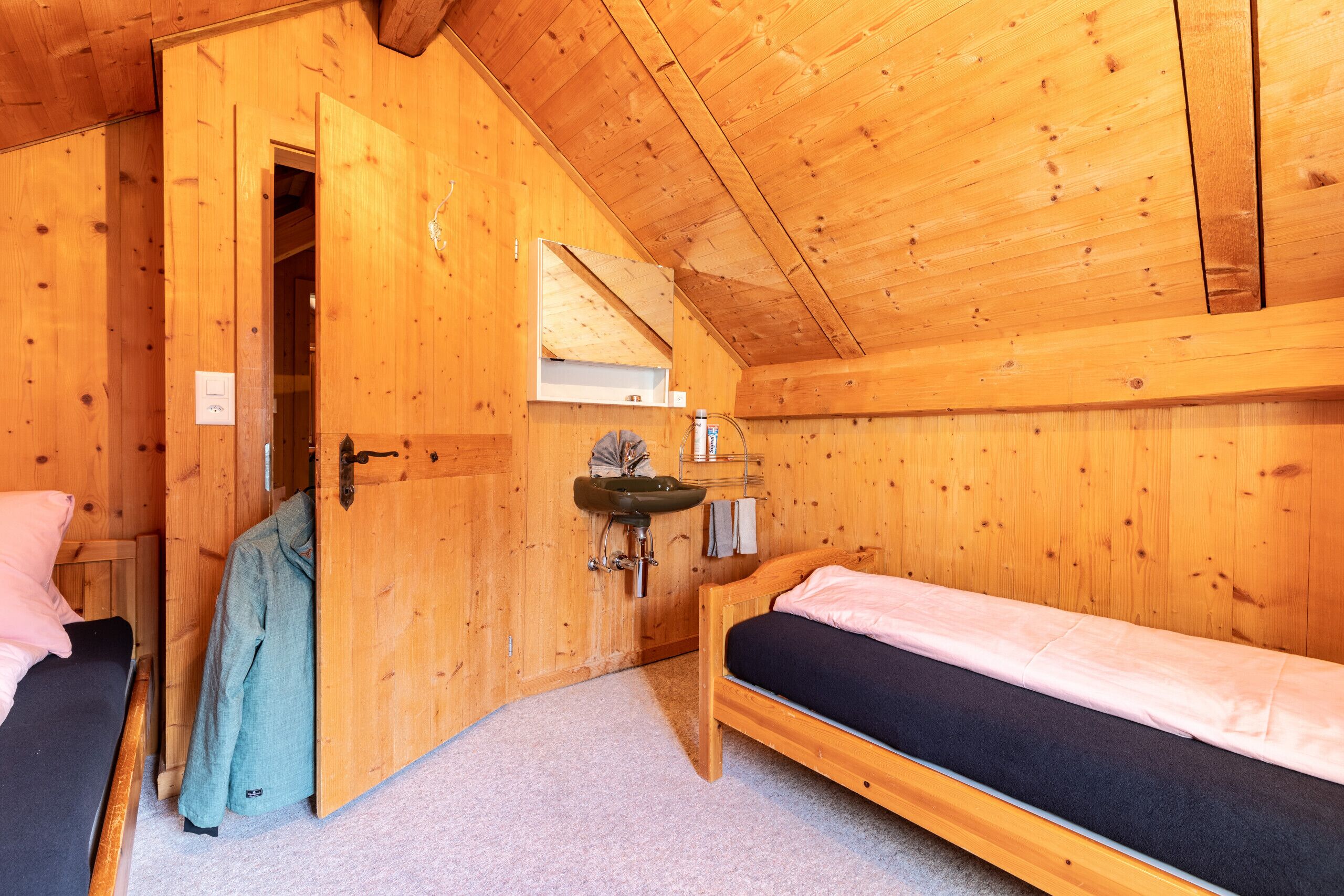 A wooden cabin room with two beds, a wooden door, a small sink, and a window.