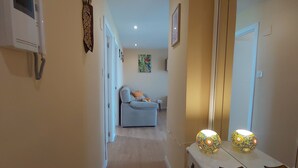 A hallway with a light blue sofa, a white console table with decorative items, and a large mirror.