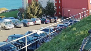 A parking lot with several cars, a grassy area, and a building with red and white walls.
