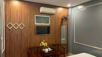 A hotel room with a wooden wall panel, a bed, a desk with chairs, a mirror, and an air conditioning unit.