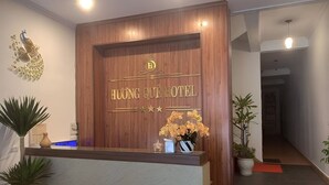The reception area of Huong Que Hotel with a wooden reception desk, a peacock decoration, and potted plants. - Huong Que Hotel HN - by BAY LUXURY (Hanoi)