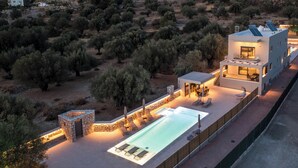 Una villa moderna con piscina, mobiliario exterior y una construcción de piedra.
