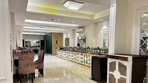 Un amplio vestíbulo de hotel con una larga recepción, un área de comedor con sillas y un suelo pulido.