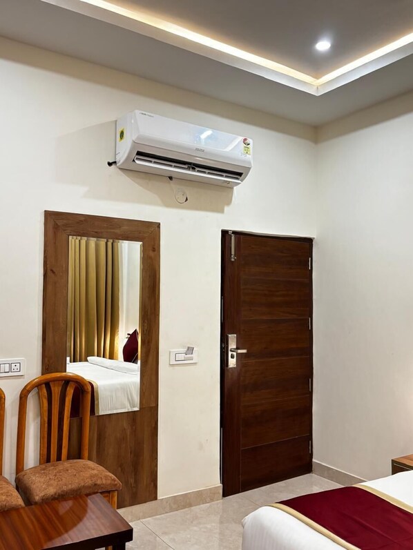 Habitación de hotel con cama, una silla de madera, una mesita pequeña, unidad de aire acondicionado y una puerta.