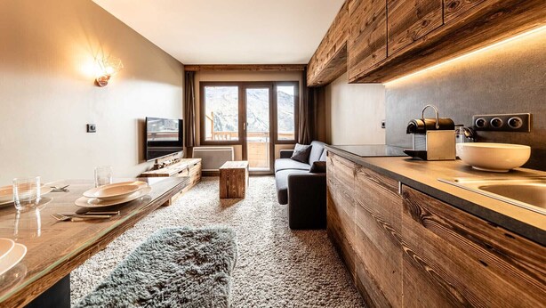 Eine kompakte Küche mit Holzausbau, einem eingebauten Backofen und einem großen Fenster mit Blick auf eine gebirgige Landschaft.