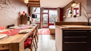 Ein Essbereich mit einem Holztisch, gedeckt für vier Personen, einem Fernseher auf einer Kommode und Bergblick durch ein großes Fenster.
