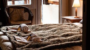 Ein gemütliches Zimmer mit einem Bett, einem Sessel, einer Lampe und Blick auf eine Holzterrasse und Berge.