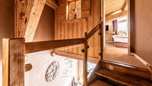 Eine Holztreppe mit Holzgeländer führt zu einem Schlafzimmer mit einem Bett, einer Kommode und einem Fenster.