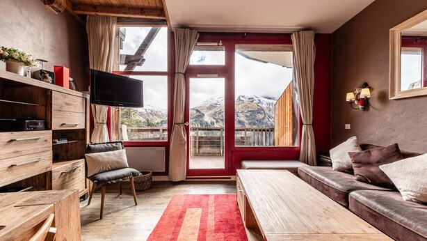 Ein gemütliches Zimmer mit einer Holzbank, einem Sofa, einem Fernseher und einem großen Fenster mit Blick auf die Berge.