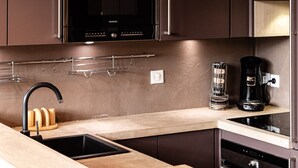 Eine moderne Küche mit dunklen Schränken, einer Edelstahl-Dunstabzugshaube, einem Einbauofen, einem Spülbecken mit schwarzem Wasserhahn und einer Kaffeemaschine.