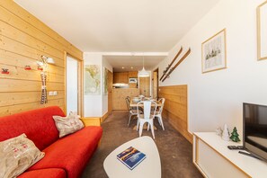 Un salon chaleureux avec un canapé rouge, une table basse blanche, un téléviseur et un coin repas comprenant une table et des chaises.