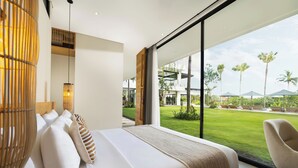 Une chambre moderne avec un grand lit, une vue sur une pelouse bien entretenue et des palmiers, ainsi qu’une grande fenêtre.