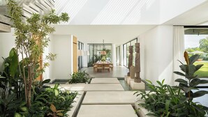 Un intérieur moderne avec un espace de repas central, entouré d’une végétation luxuriante et offrant une vue sur l’extérieur.
