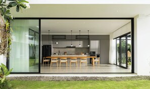 A modern kitchen with a large island, built-in appliances, and a sliding glass door leading to a patio. - Arita Villa Canggu by Nakula (Canggu)