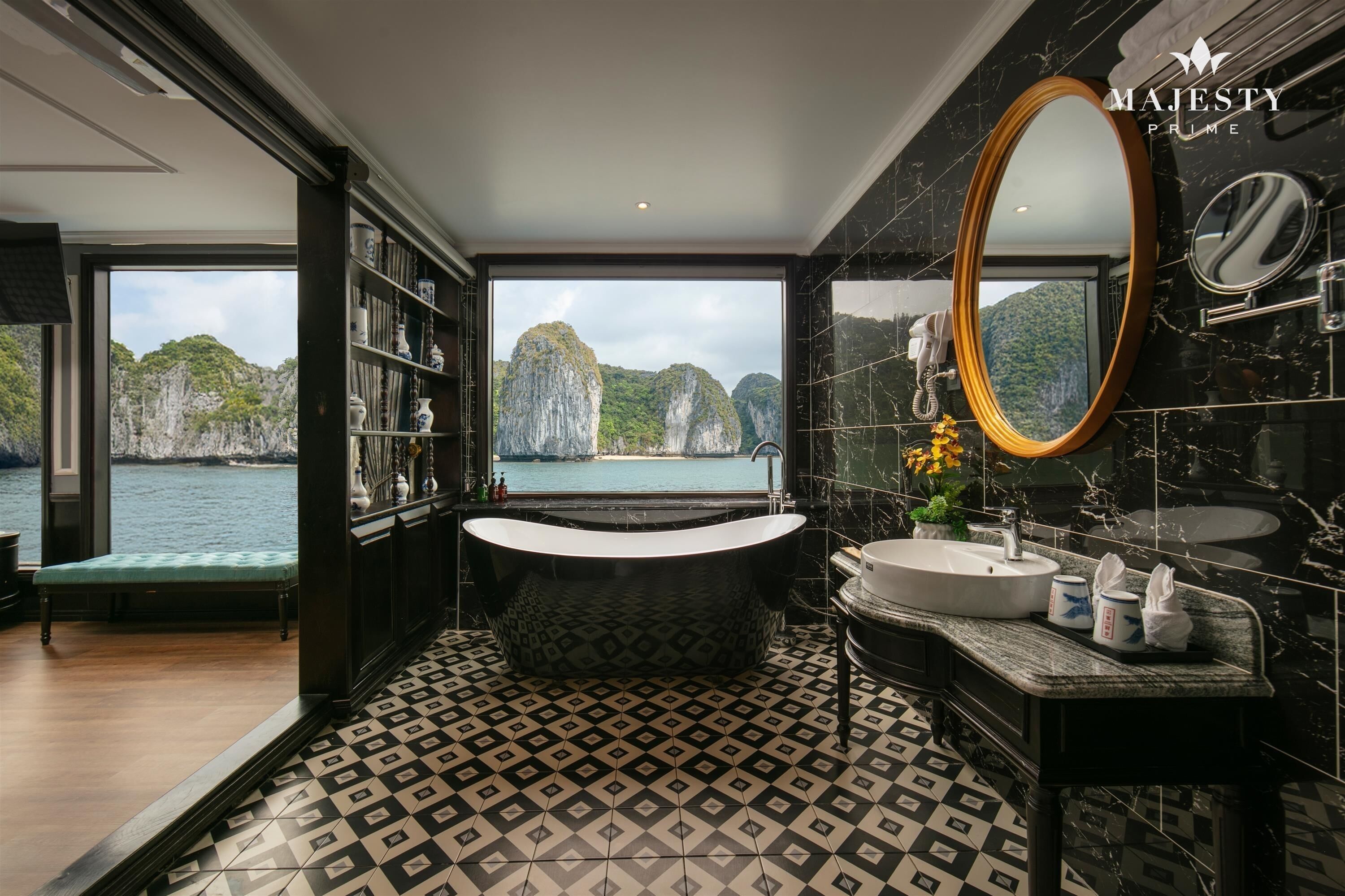 A luxurious bathroom with a bathtub, sink, and large mirror, featuring a view of a mountainous landscape and a body of water.