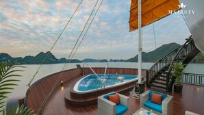 Ein luxuriöses Bootsdeck mit Whirlpool, Korbmöbeln und einer Treppe zu einem oberen Deck.