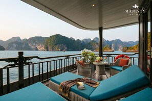 A deck with wicker furniture, a table with a vase of flowers, and a book titled "COBBY". - Majesty Prime Cruise (Tuan Chau)