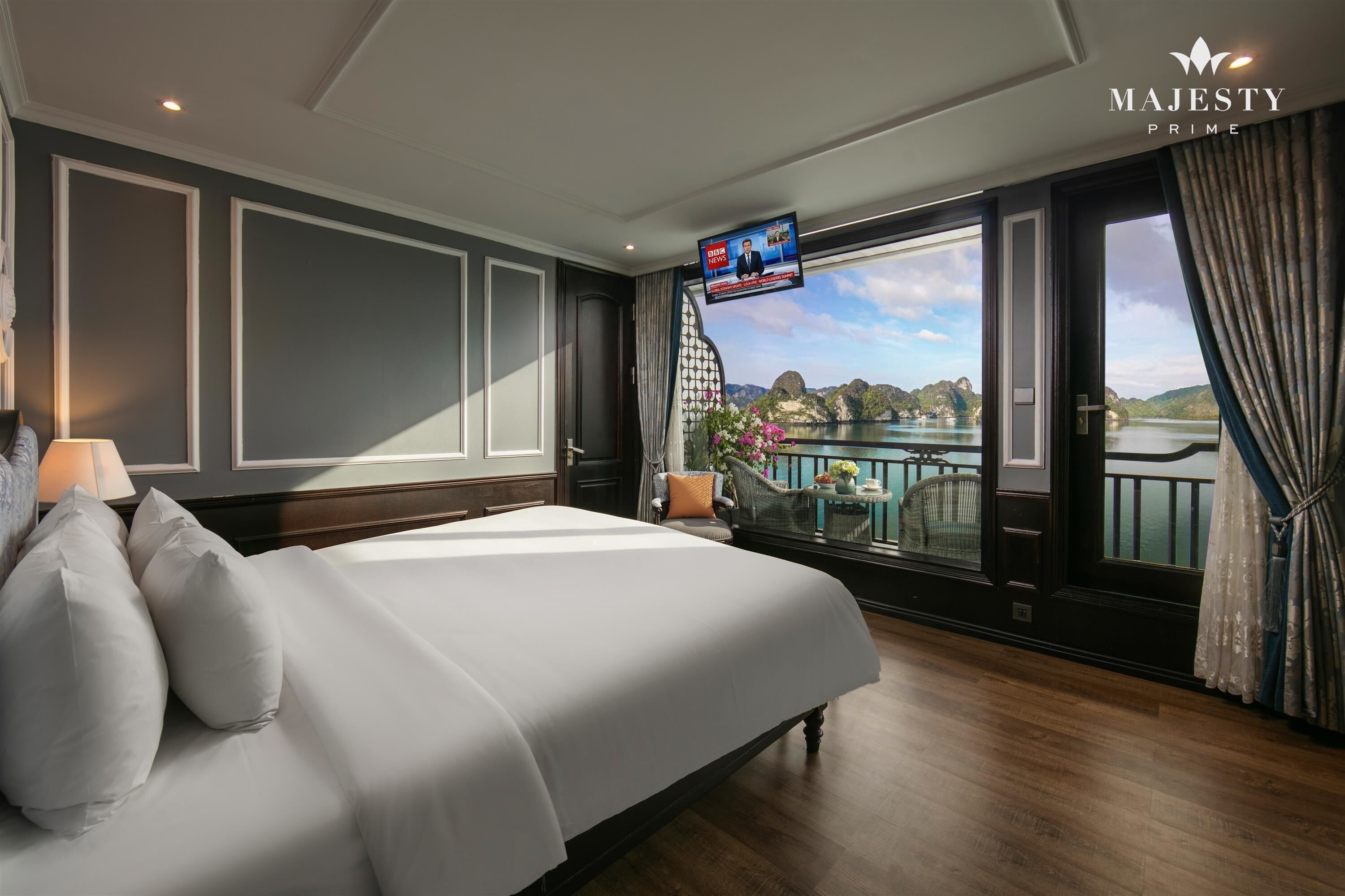 Un dormitorio amplio con una cama grande, un televisor montado en la pared y un balcón con vistas a un lago y montañas.