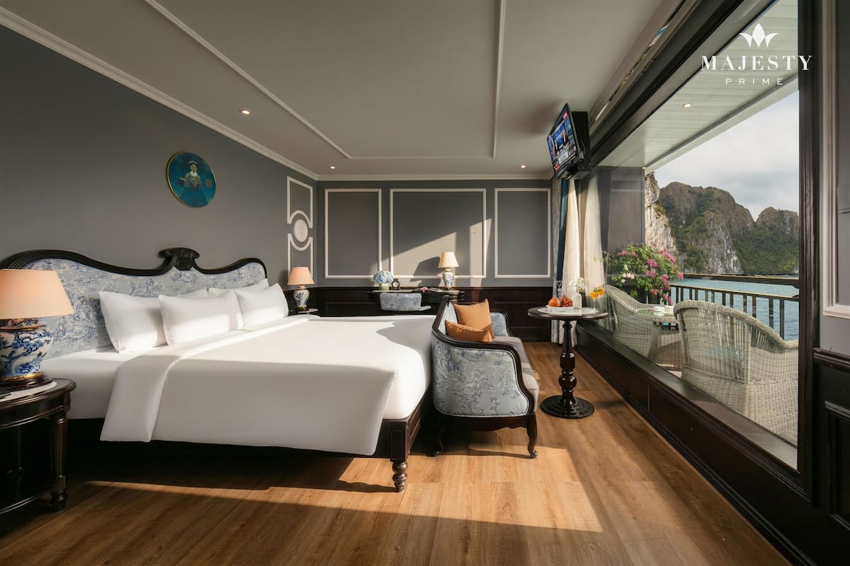 A spacious bedroom with a large bed, a sitting area with a chair and table, and a balcony with a view of the mountains.