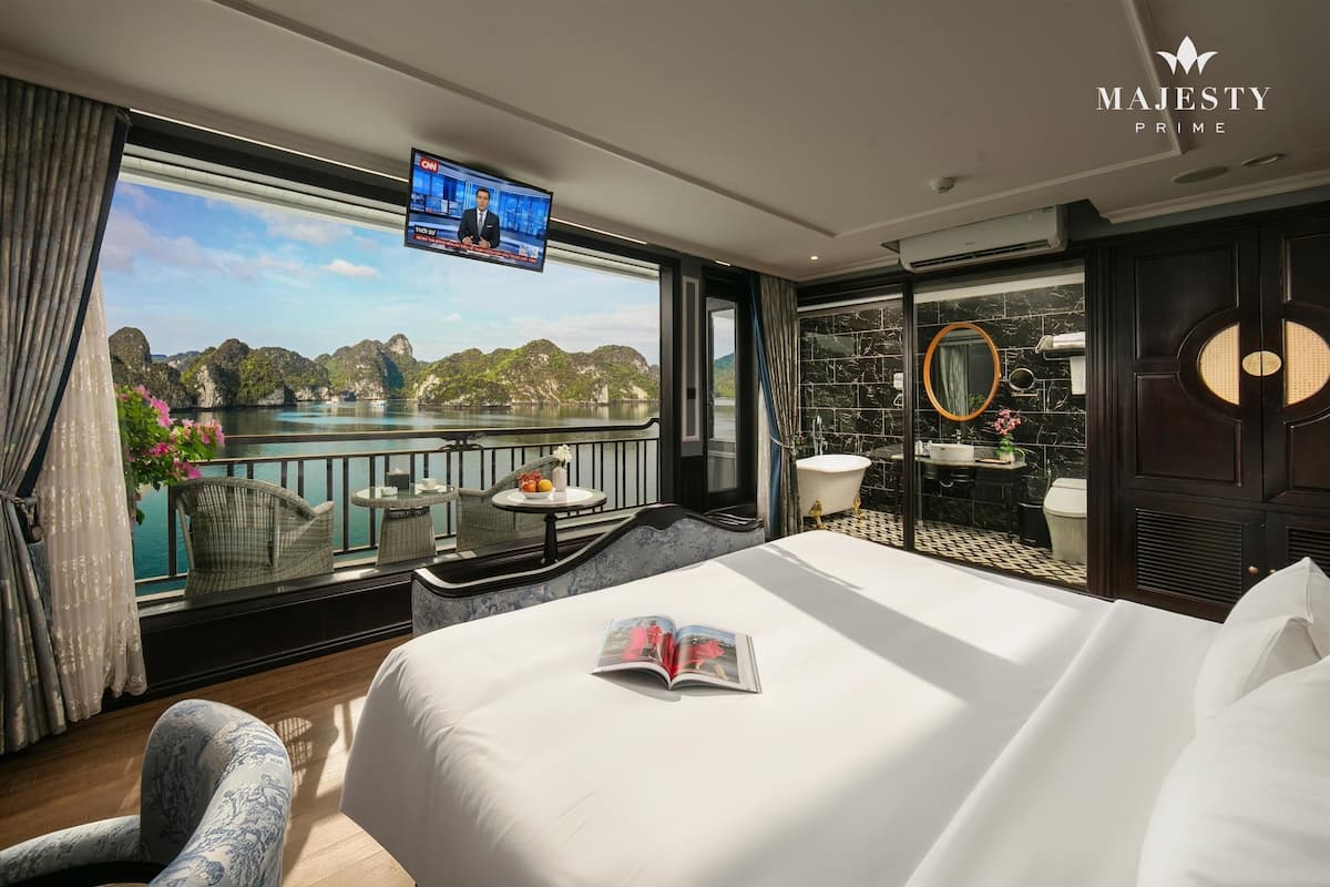 A hotel room with a large bed, a TV, a balcony with a view of the sea, and a bathroom with a marble floor.
