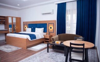 Quarto de hotel com uma cama, uma escrivaninha, uma cadeira e uma mesinha.