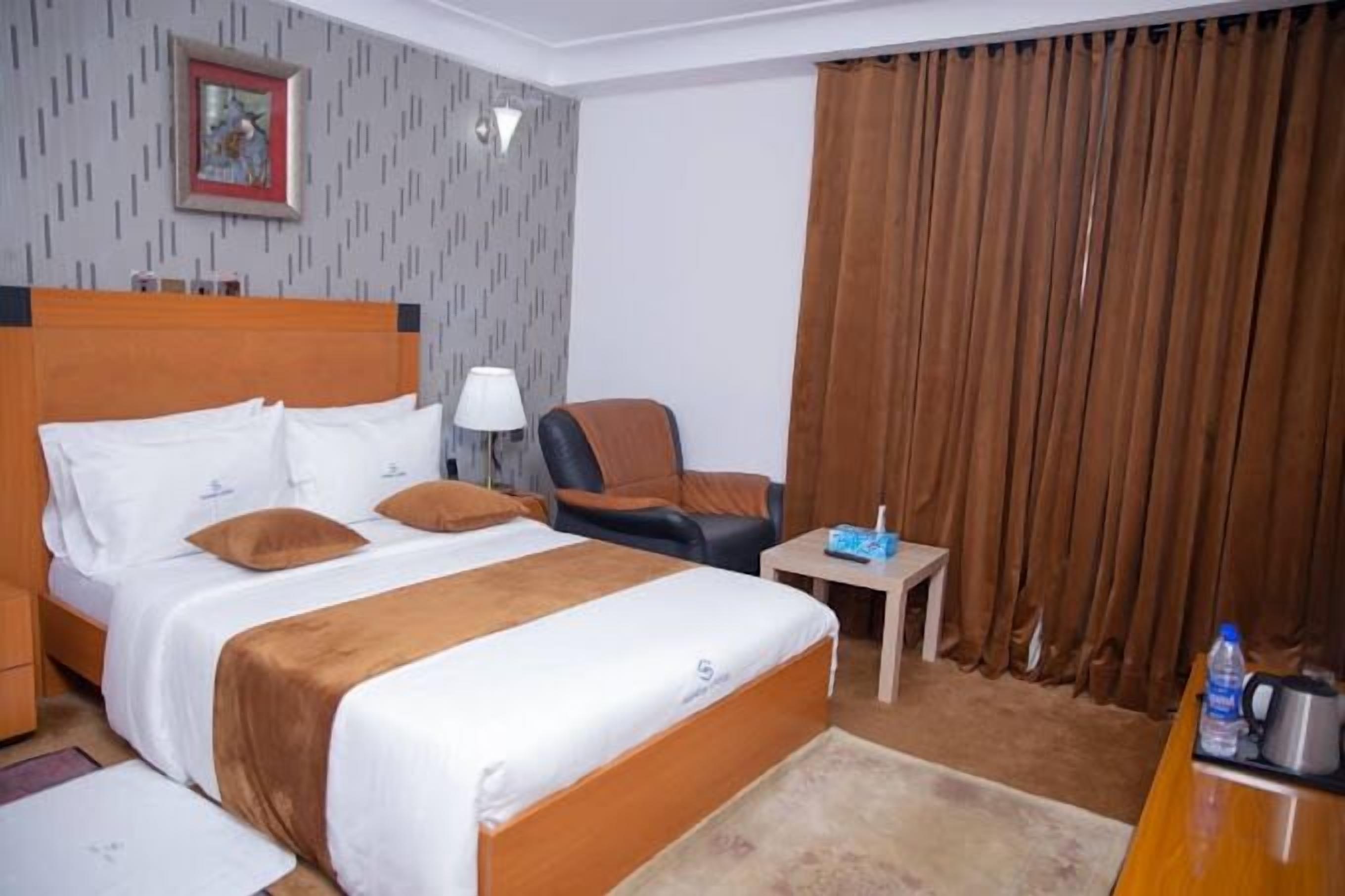 Una habitación de hotel con una cama grande, una silla, una mesita y una cortina.
