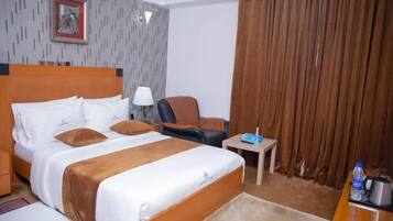 Una habitación de hotel con una cama grande, una silla, una mesita y una cortina.
