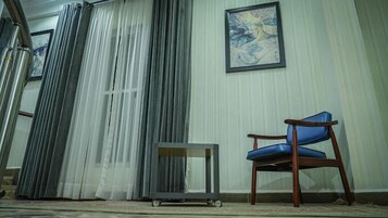 Um quarto com uma cadeira azul, uma mesinha e uma janela grande com cortinas.