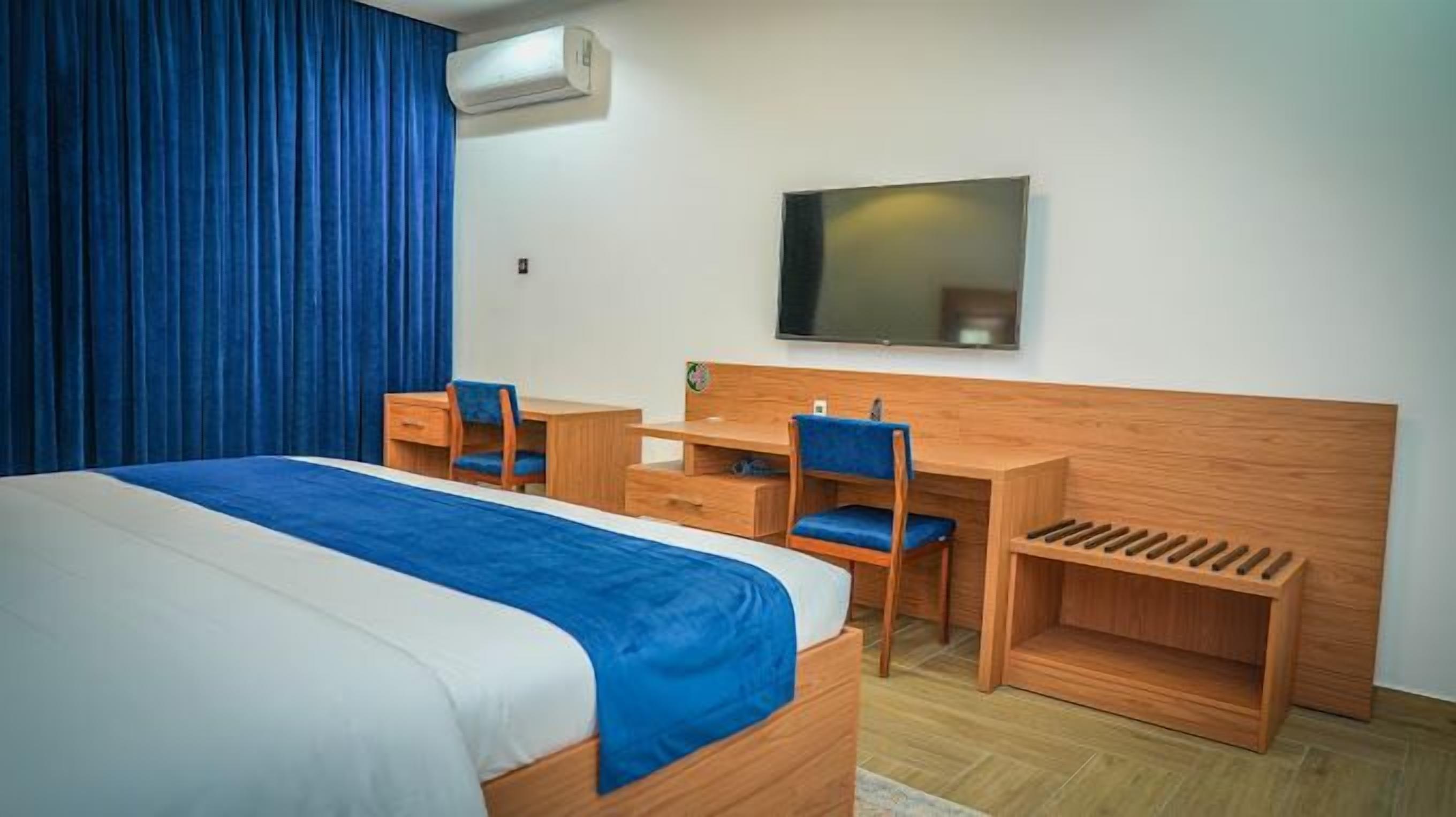 A hotel room with a bed, a desk, a chair, a TV, and a window with curtains.