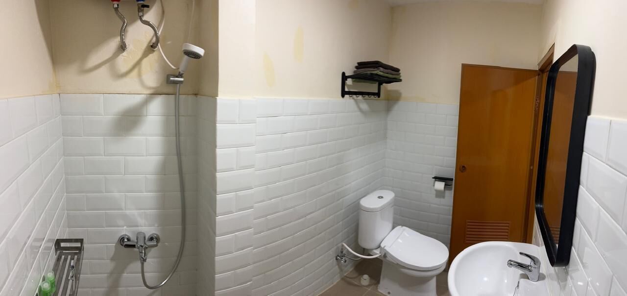 Une salle de bain avec des murs carrelés de carreaux blancs, une douche, des toilettes et un lavabo.