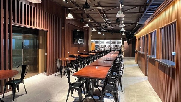A long dining table with chairs, wooden paneling, and pendant lighting in a spacious room. - Kostkan House (Jakarta)
