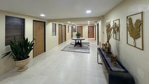 A hotel hallway with a central round table, potted plants, and decorative wall art. - Kostkan House (Jakarta)