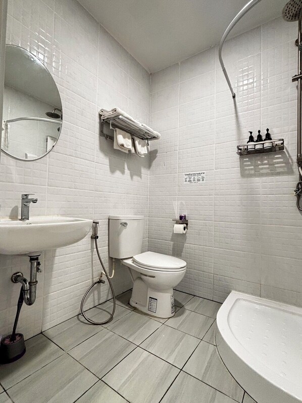 A modern bathroom with white tiles, a round mirror, a toilet, a sink, and a shower. - PJ Hostel & Bar (Pattaya)