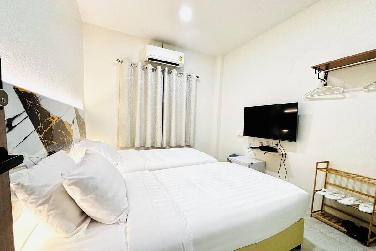 Hotellihuone, jossa on suuri sänky, seinälle asennettu taulutelevisio ja pieni pöytä, jossa on lamppu.