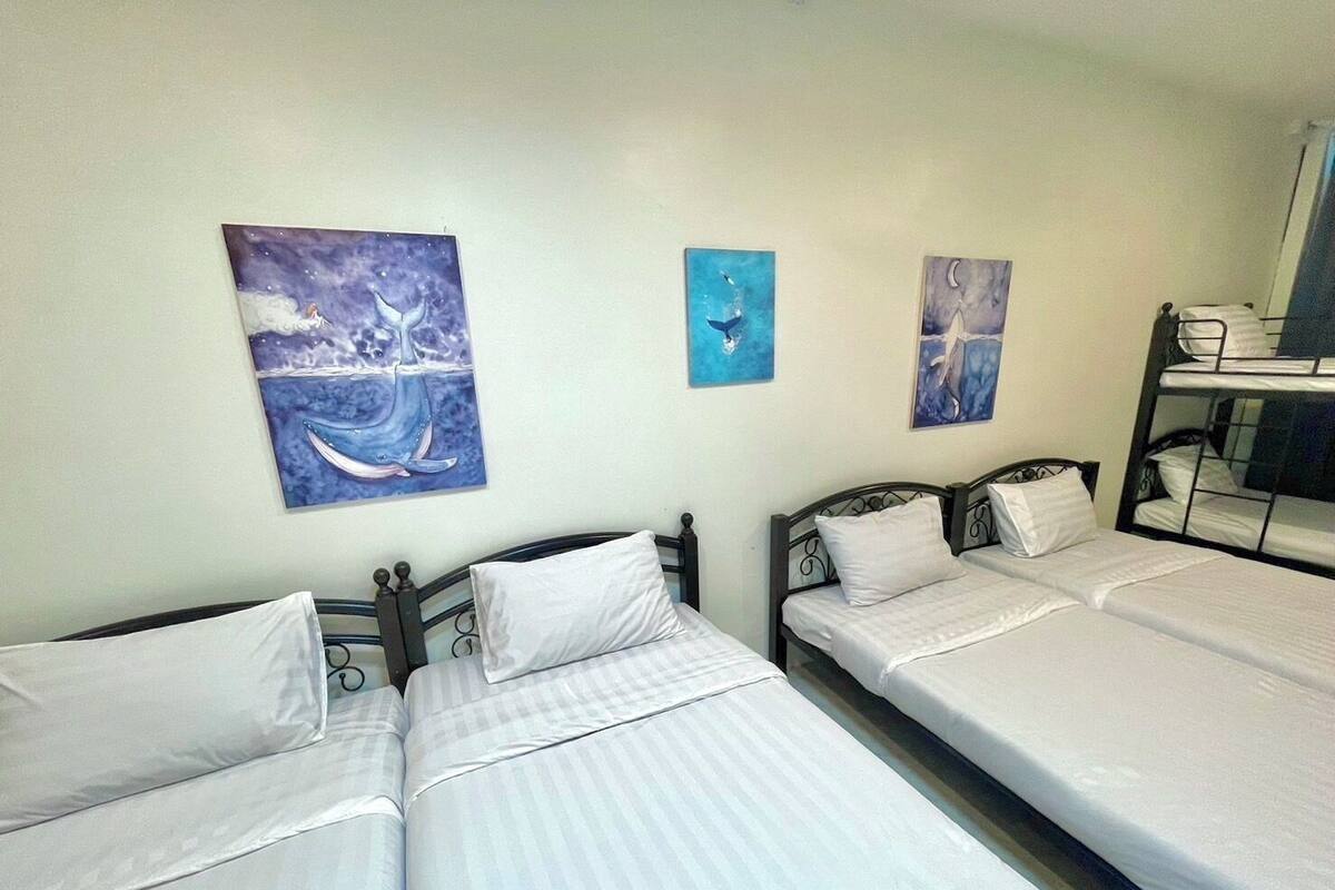 Hotellihuone, jossa on kaksi erillistä sänkyä, kerrossänky ja kolme seinätaulua.