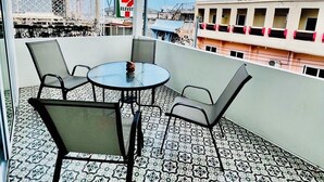 Un balcón con suelo estampado, una mesa redonda con sillas y vistas a edificios al fondo.