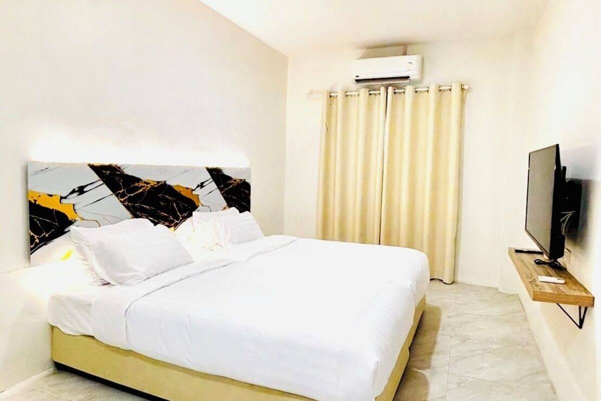 Moderni hotellihuone, jossa on suuri sänky, litteänäyttöinen televisio puutelineessä ja ilmastointilaite seinällä.