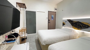 Una habitación de hotel con dos camas, televisor, escritorio y una puerta con un cartel.