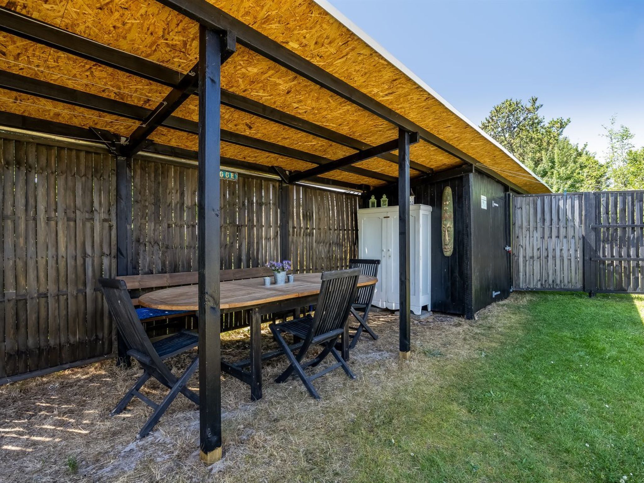 An outdoor patio with a wooden table and chairs, a covered seating area, and a fenced yard.