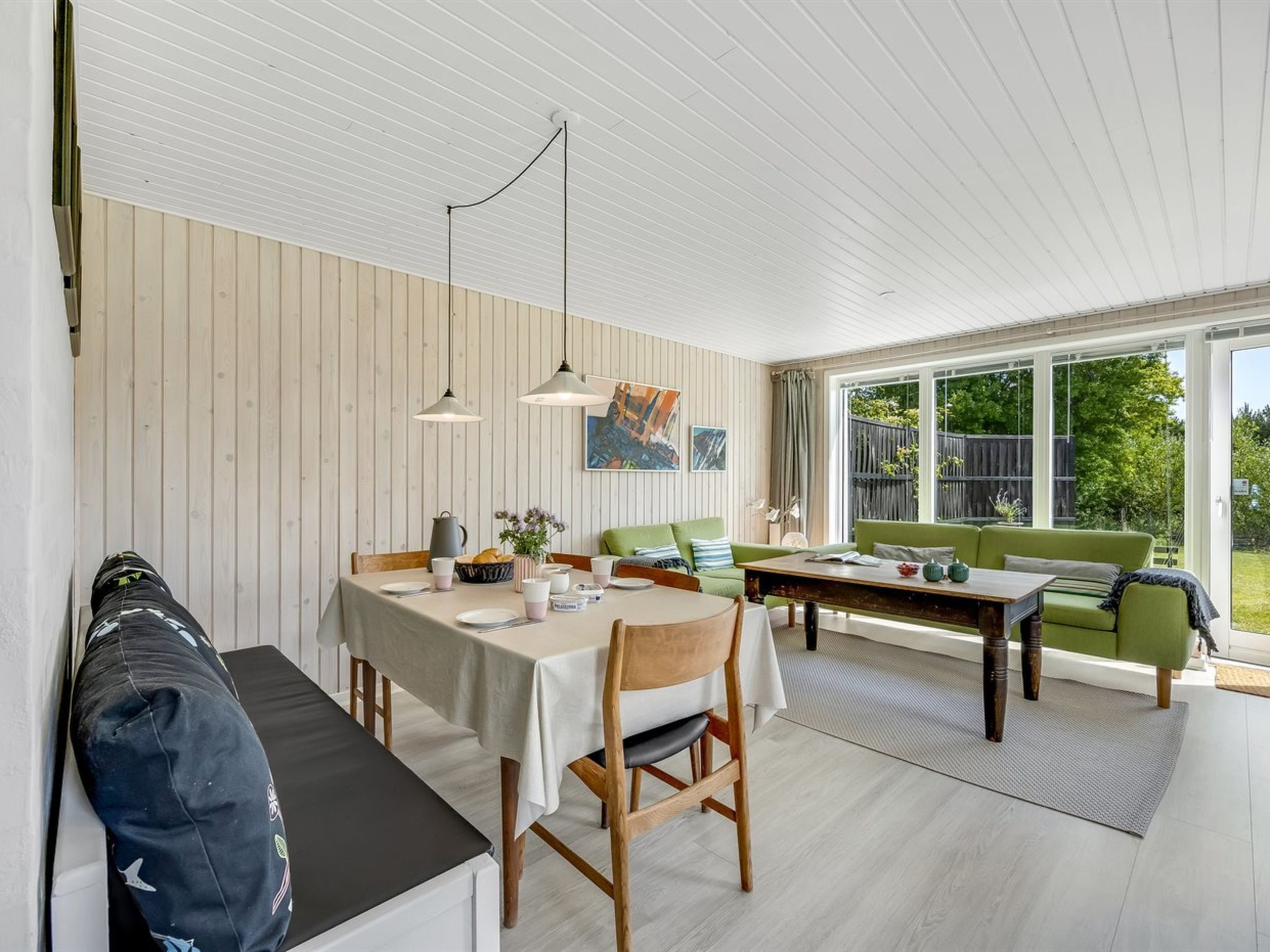 Et spiseområde med et bord dækket til fire personer, en grøn sofa og en bænk med en rygsæk.