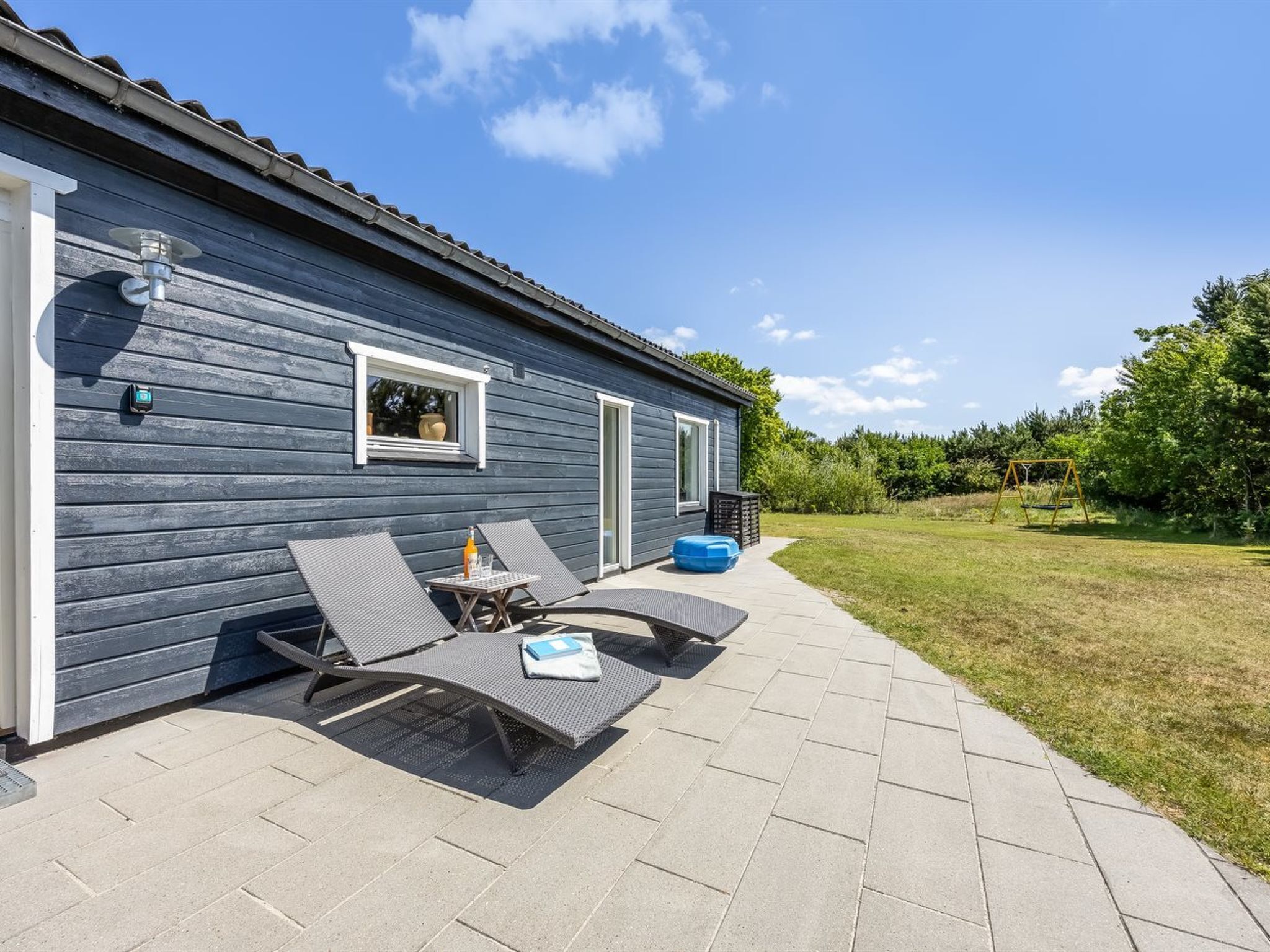 Une maison dotée d’un patio comprenant deux fauteuils de jardin et une petite table, ainsi qu’une fenêtre et une porte.