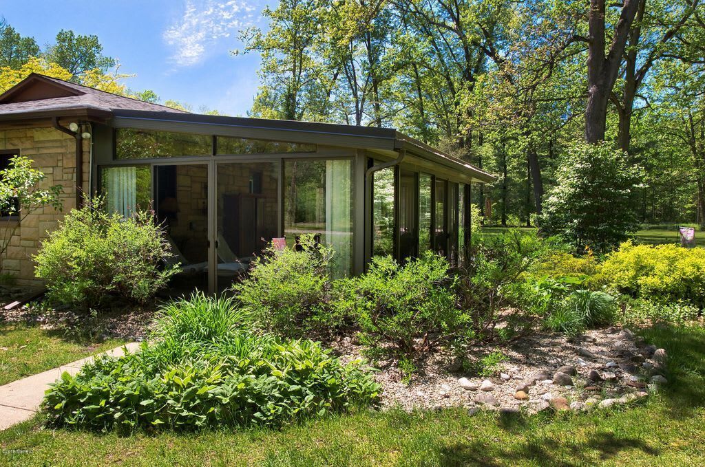 A house with a glass-enclosed porch surrounded by a well-maintained garden with various shrubs and a stone pathway.