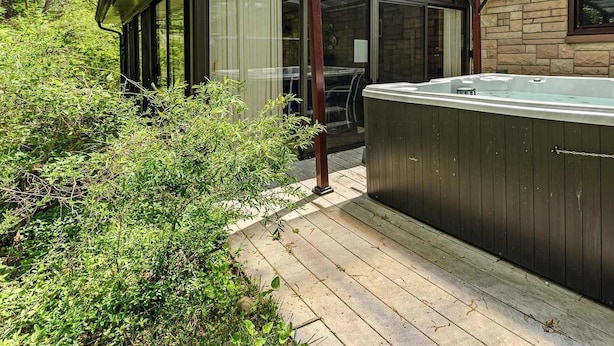 Un bain à remous avec une terrasse en bois, un patio vitré et un mur en pierre.