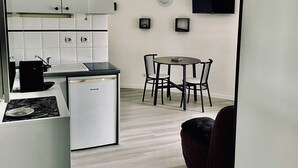 A compact kitchen with white cabinets, a small refrigerator, and a dining area with a table and chairs. - Bright apartment, quiet, secure residence, swimming pool/parking, near Port Minimes (La Rochelle)