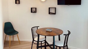 A modern dining area with a round wooden table, four black chairs, and a flat-screen TV mounted on the wall. - Bright apartment, quiet, secure residence, swimming pool/parking, near Port Minimes (La Rochelle)