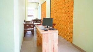 A room with a wooden desk, a computer, and a chair. There is a wall with a grid pattern and a door in the background. - Pudan Residence Balige By Helocus (Balige)
