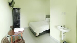 A small, clean room with a bed, a chair, a table, a mirror, and a sink. - Pudan Residence Balige By Helocus (Balige)