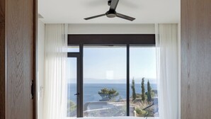 A bedroom with a large window, a ceiling fan, and a bed with white bedding. - Villa Apollo Porto Cheli (Ermionida)