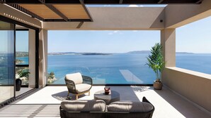 A modern balcony with a view of the sea, furnished with a sofa and chairs, and a potted plant. - Villa Apollo Porto Cheli (Ermionida)
