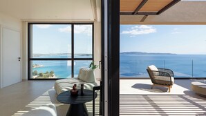 A modern living room with a large sliding glass door leading to a balcony with a view of the sea. - Villa Apollo Porto Cheli (Ermionida)